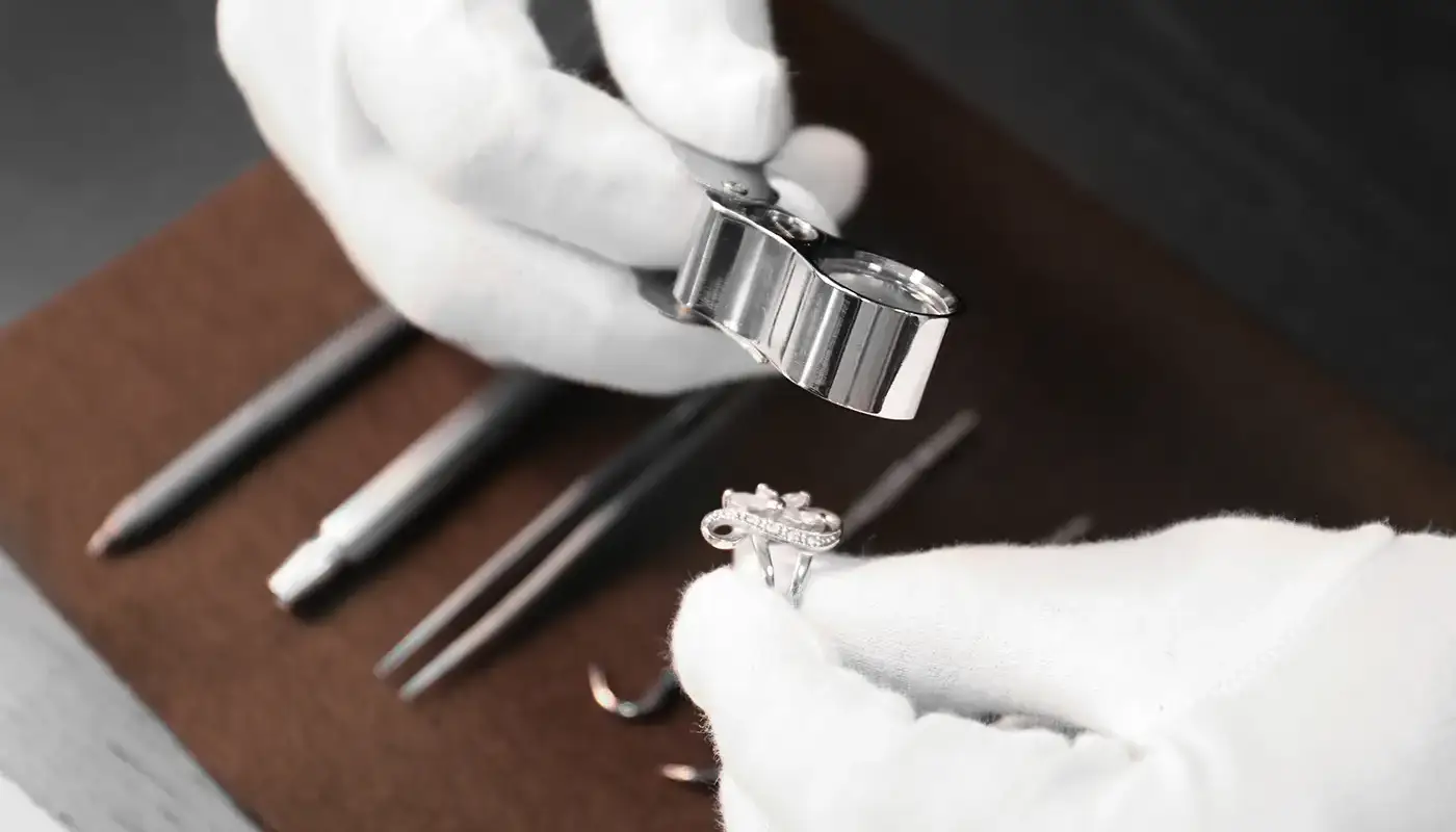 Hands in white gloves inspecting jewelry with magnifying tool during appraisal at Manning Jewelry