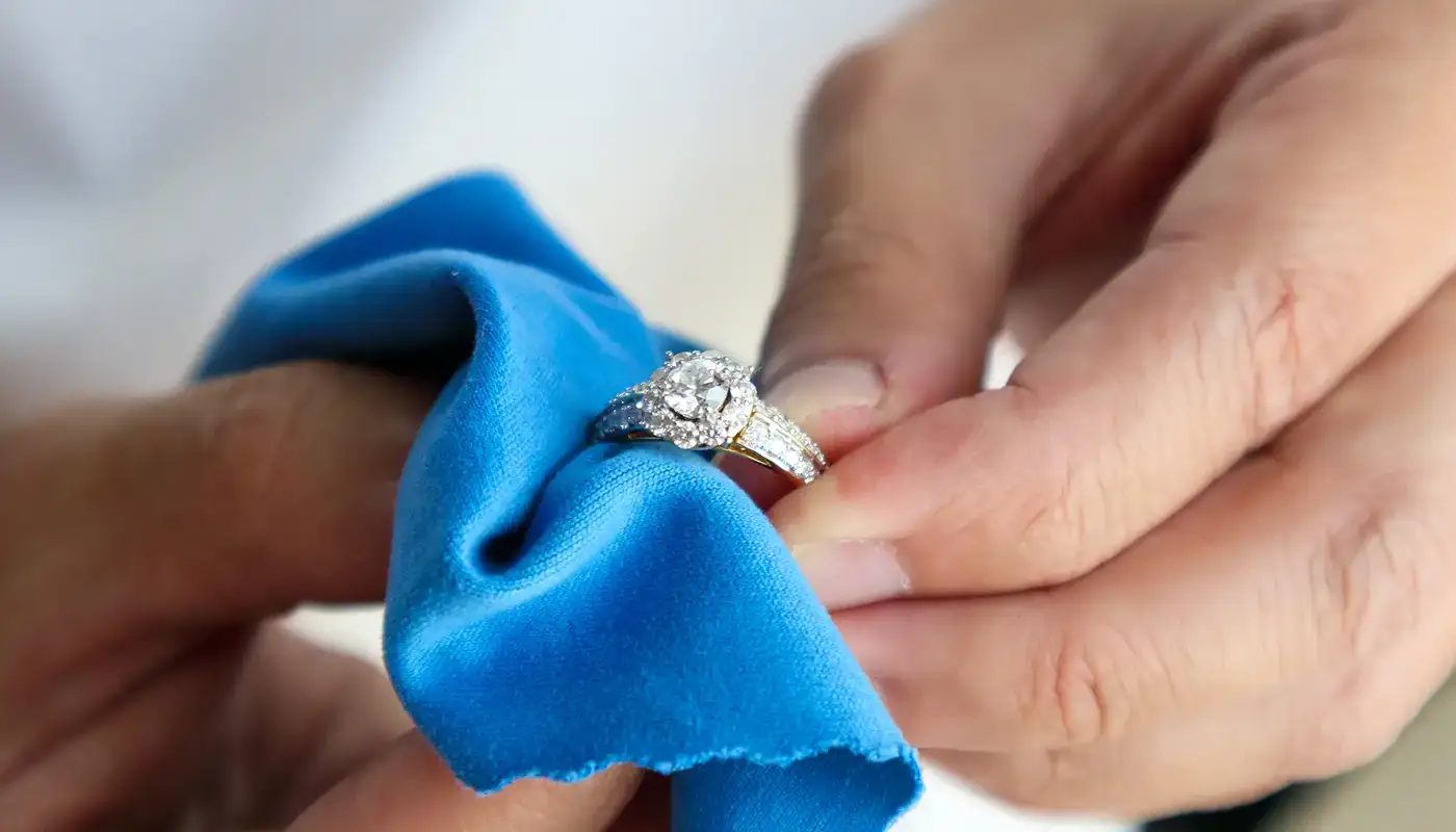 Hands using blue cleaning cloth to polish diamond ring at Manning Jewelry