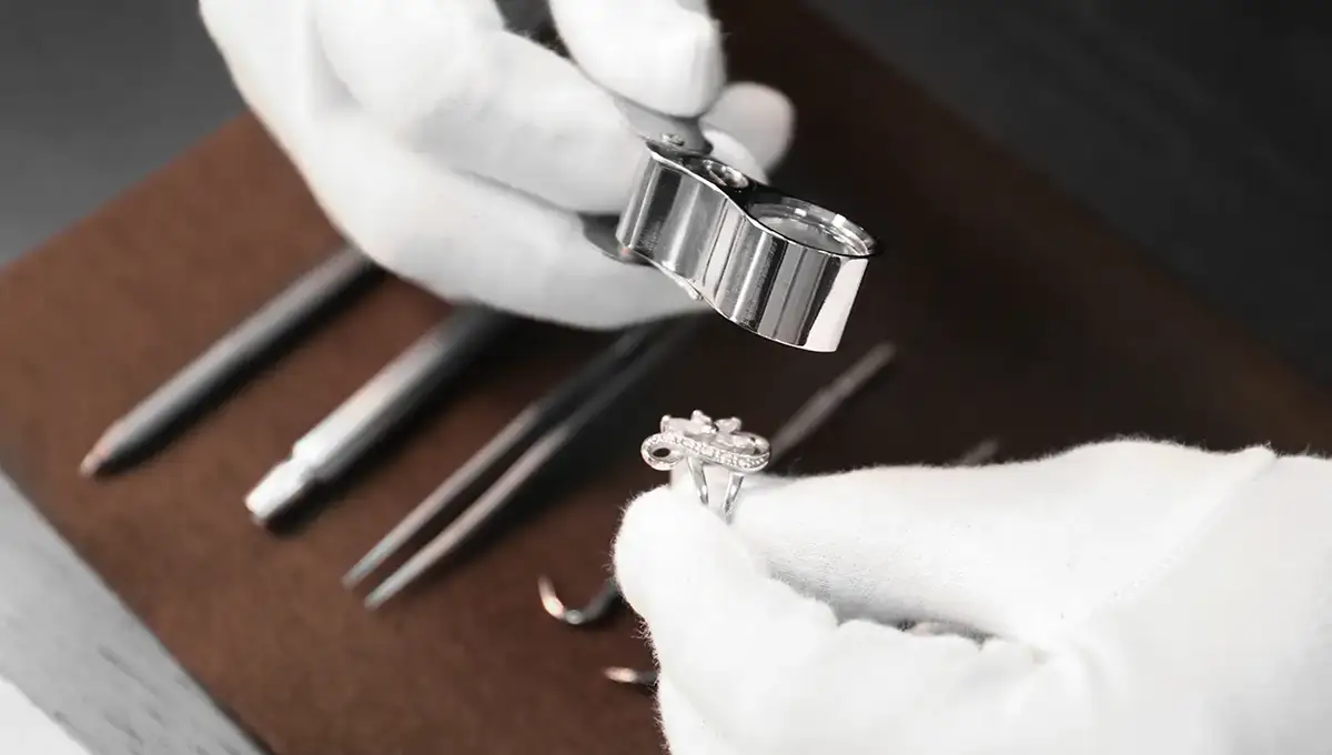 Hands in white gloves inspecting jewelry with magnifying glass and other appraisal tools at Manning Jewelry